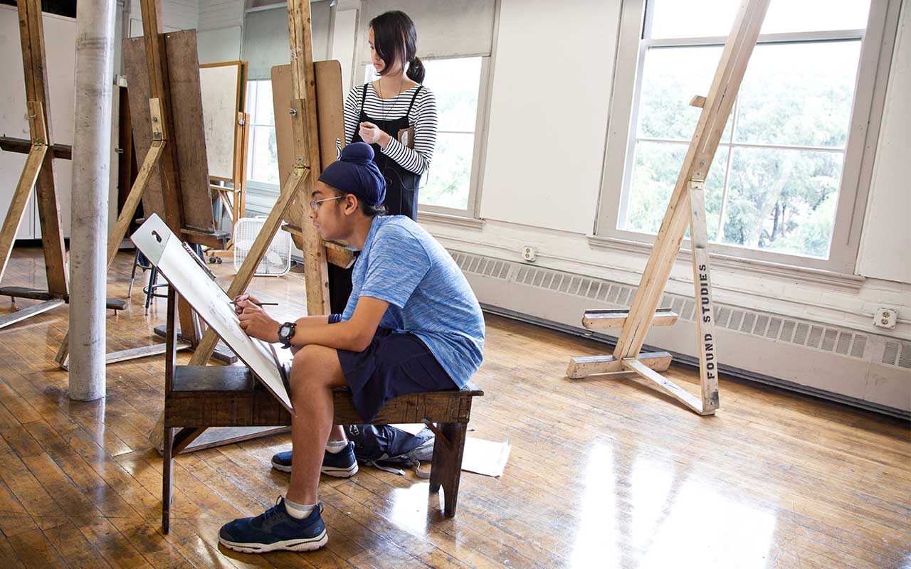 Teen students working with easels in drawing studio.