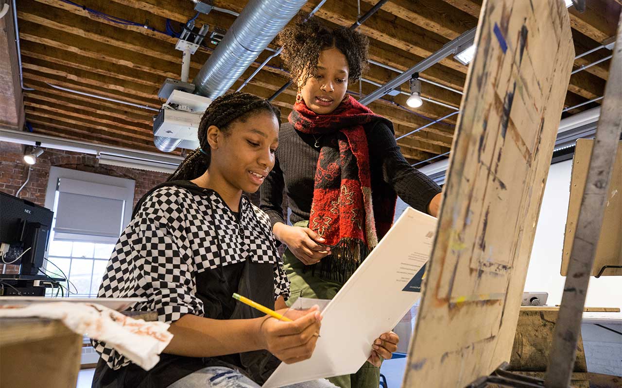 Teen student and instructor working at an easel in a drawing studio.