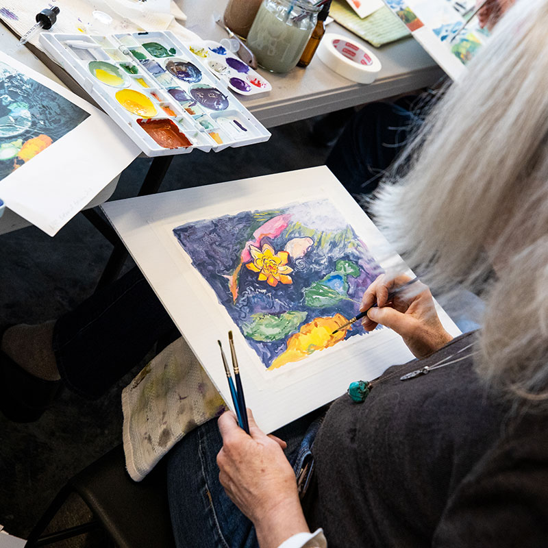 A woman works on a painting using gouache.