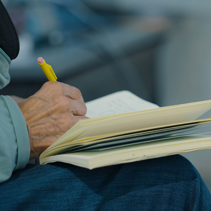 A person writes with a pencil in a journal.