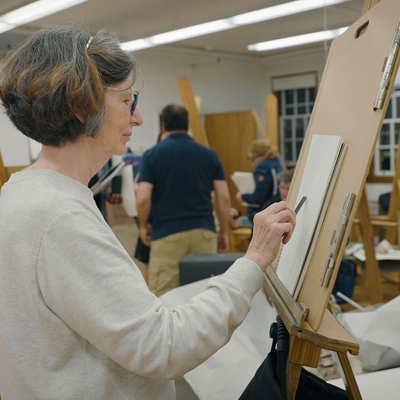 A woman draws on a drawing board in an art classroom.