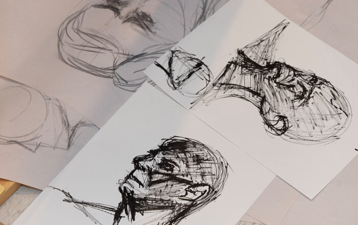 A collection of portrait drawings in charcoal lay on a table.