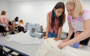 student and instructor standing at a table with fabric and sewing machine