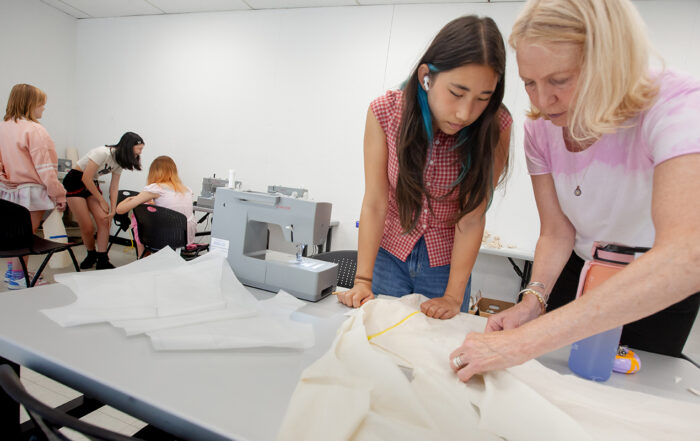 students and instructor standing at a table with fabric and sewing machine