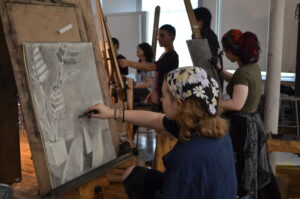 a student sits at an easel drawing with charcoal