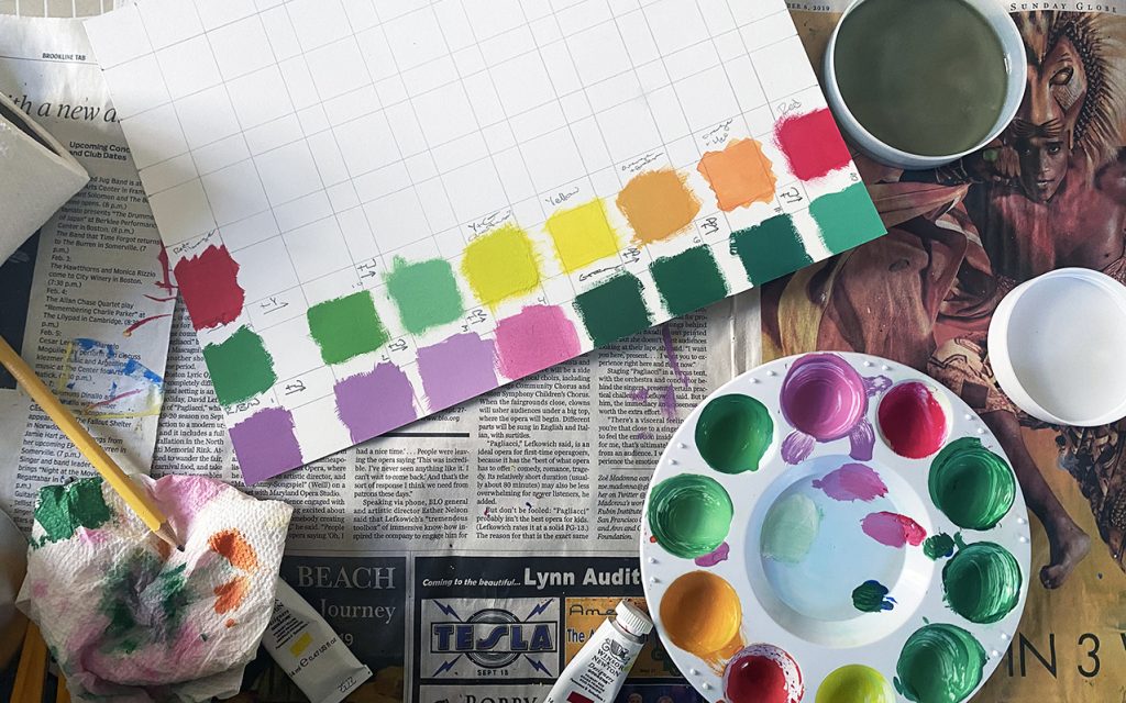 photograph of paint palette, color swatches, and paint cup on newspaper