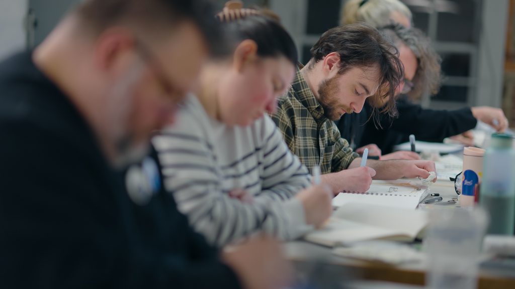 students sitting at a table drawing in sketchbooks