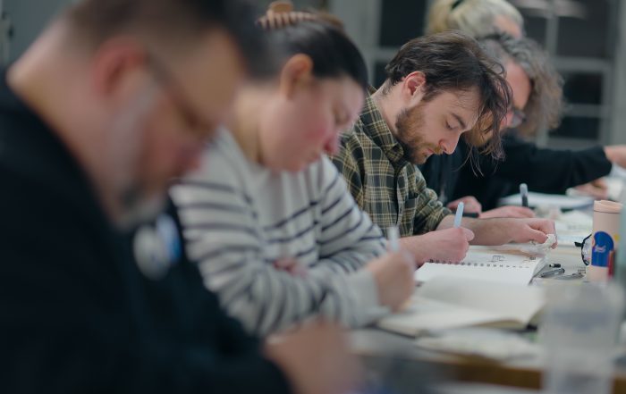students sitting at a table drawing in sketchbooks