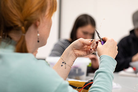 design student working on a jewelry piece holding pliers