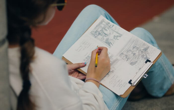 A teen art student at RISD sitting outside drawing with pencil and paper during a Landscape Drawing class.